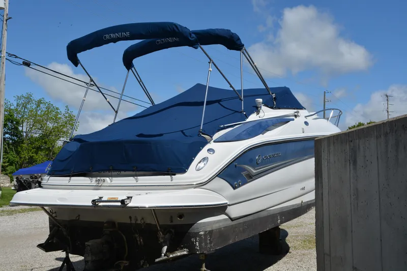 Slide: The Image of 2004 Crownline 270 CR boat with blue cover, parked on a gravel surface under a clear sky. - 13