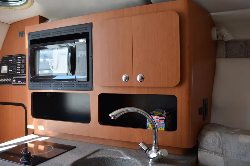 Slide: The Image of 2004 Crownline 270 CR boat interior with microwave, sink, and wooden cabinetry. - 26