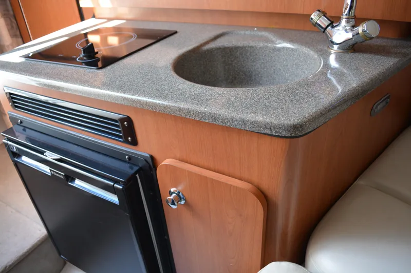 Slide: The Image of 2004 Crownline 270 CR boat interior with kitchenette, featuring sink, stove, and mini-fridge. - 27
