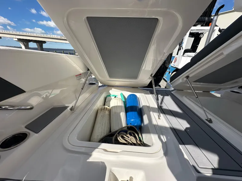 Slide: The Image of 2023 Chaparral 250 OSX boat storage compartment with fenders and ropes under a sunny sky. - 7