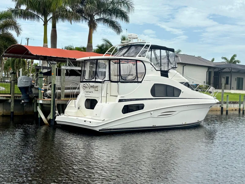 Slide: The Image of 2005 Silverton 39 Motor Yacht docked by palm trees, calm water, and a modern house. - 2