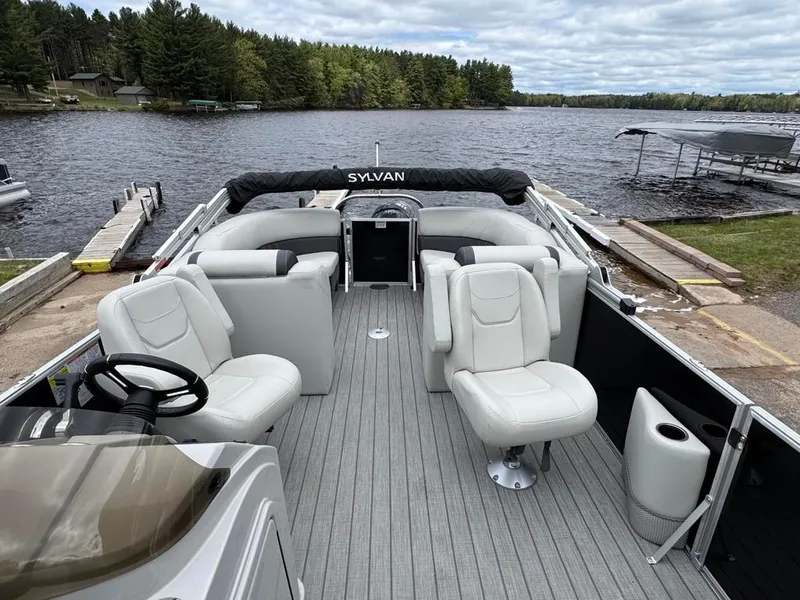 Slide: The Image of 2024 Sylvan Mirage 822 LZ pontoon boat with plush seating, docked by a scenic lake. - 14