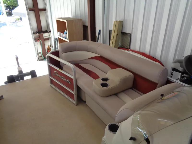 Slide: The Image of 2015 Sweetwater 2086 pontoon boat seating in storage, featuring beige and red upholstery with cup holders. - 14