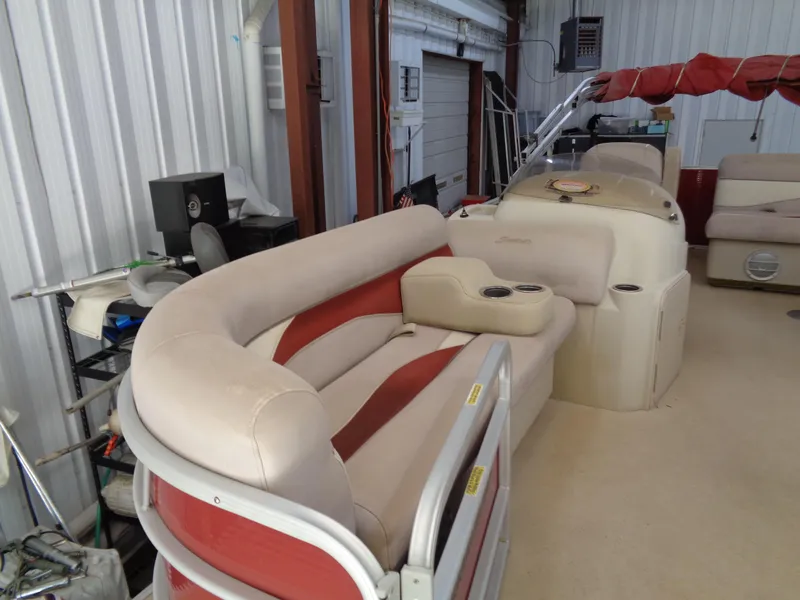 Slide: The Image of 2015 Sweetwater 2086 pontoon boat interior with beige and red seating in a storage facility. - 8