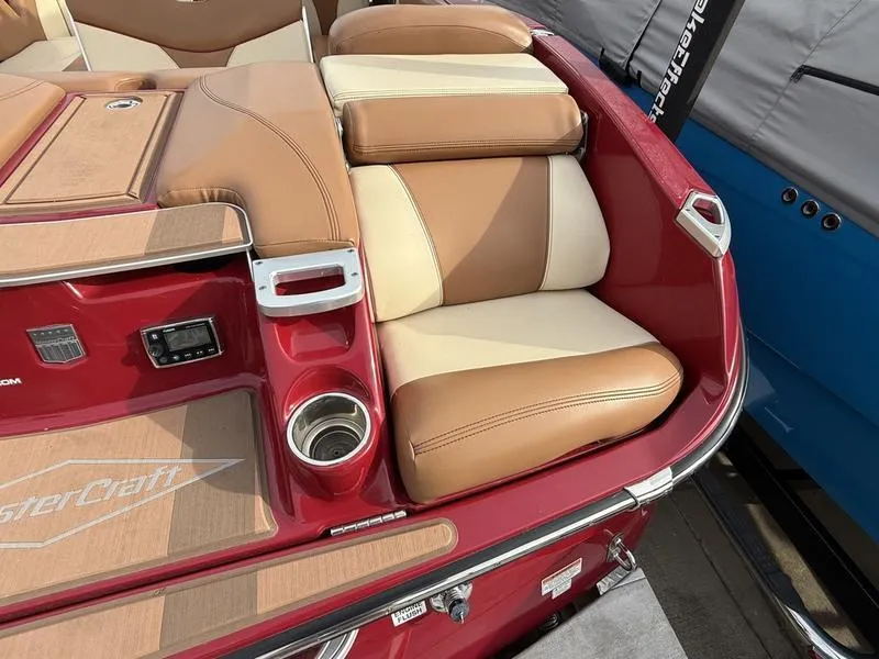 Slide: The Image of 2016 MasterCraft X23 boat interior with tan and cream seating, red accents, and cup holder. - 20