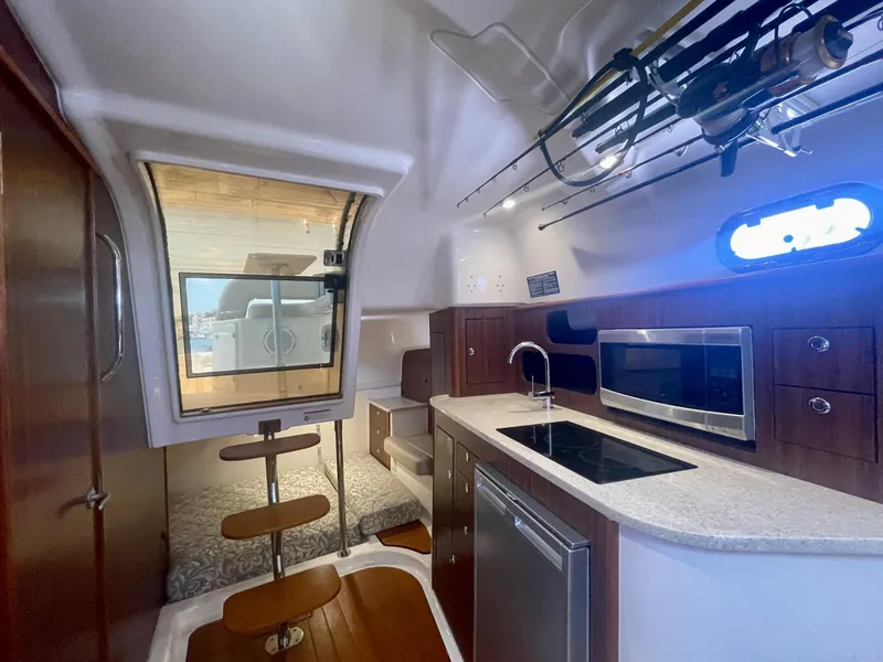 Slide: The Image of 2015 Pursuit 345 Offshore cabin interior with kitchenette, seating, and fishing rod storage. - 23