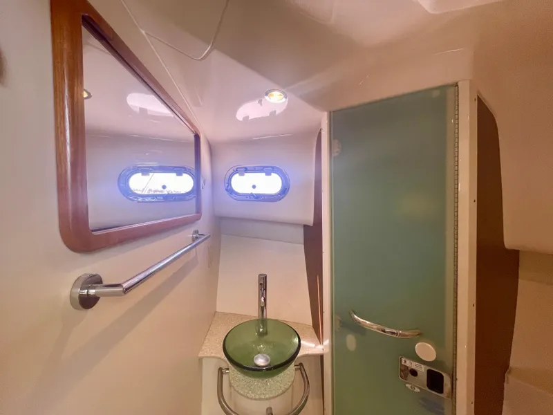 Slide: The Image of 2015 Pursuit 345 Offshore bathroom with glass sink, mirror, and porthole windows. - 31