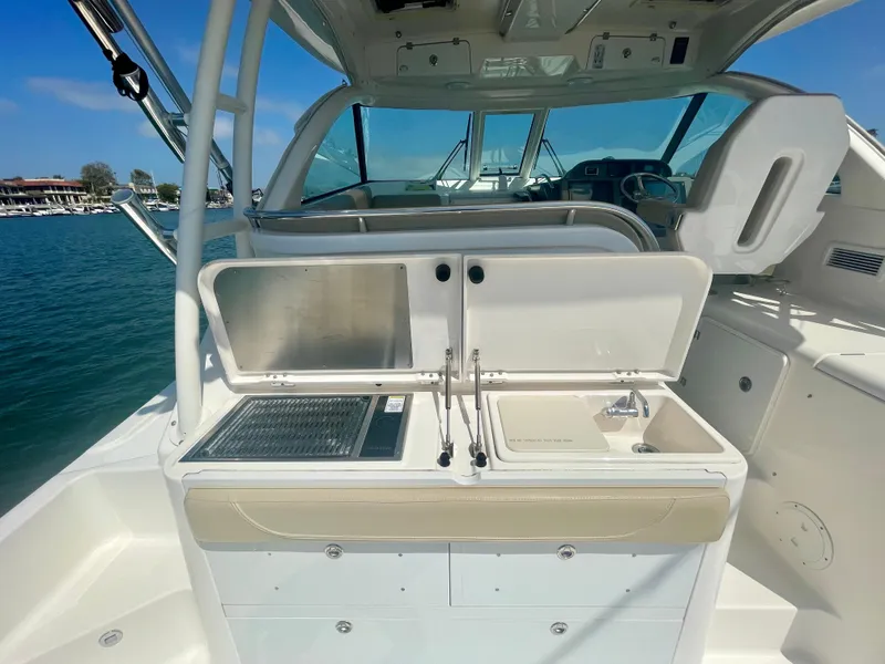 Slide: The Image of 2015 Pursuit 345 Offshore boat interior with kitchenette and sink, docked by the water. - 48