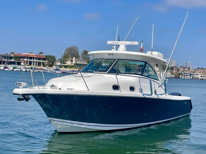Slide: The Image of 2015 Pursuit 345 Offshore boat on calm water, with coastal buildings in the background. - 6
