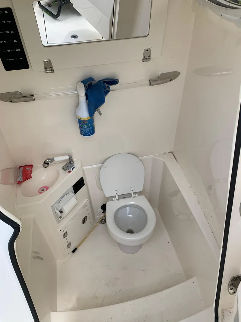 Slide: The Image of 2021 Cobia 240 CC boat bathroom with toilet, sink, and cleaning supplies. - 6