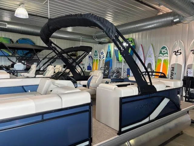 Slide: The Image of 2025 Godfrey SW2286CSE pontoon boat in showroom with surfboards in background. - 2