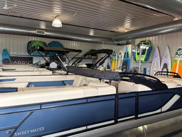 Slide: The Image of 2025 Godfrey SW2286CSE pontoon boat in showroom with surfboards and paddleboards. - 3
