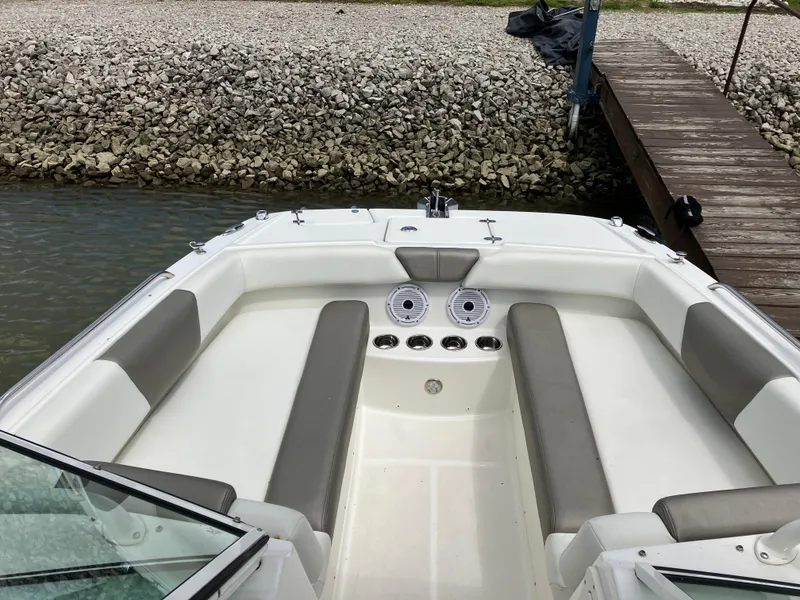 Slide: The Image of 2022 World Cat 230 SD boat interior with gray seating and cup holders, docked by a rocky shore. - 18