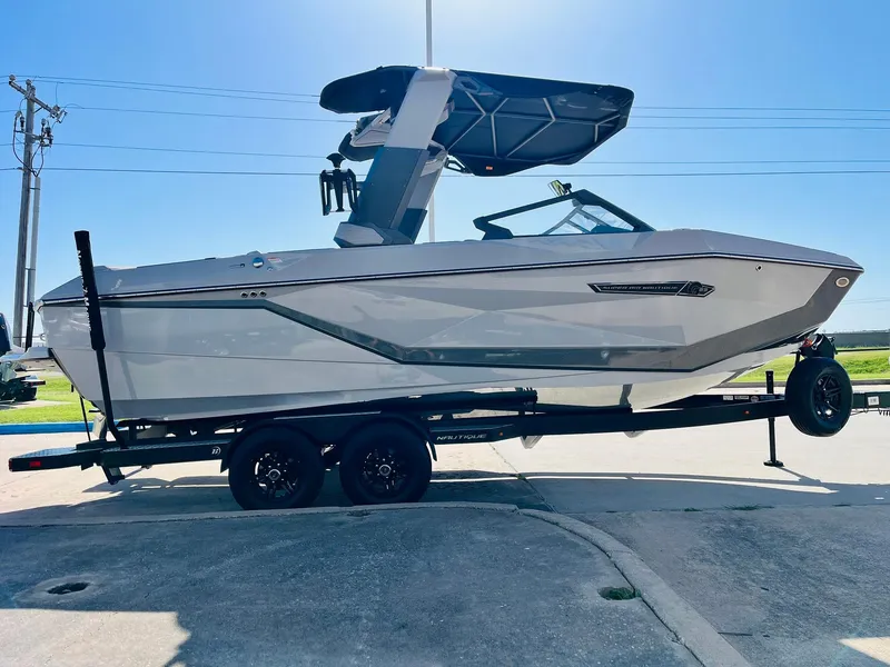 Slide: The Image of 2025 Nautique Super Air G23 boat on trailer, side view, under clear blue sky. - 3