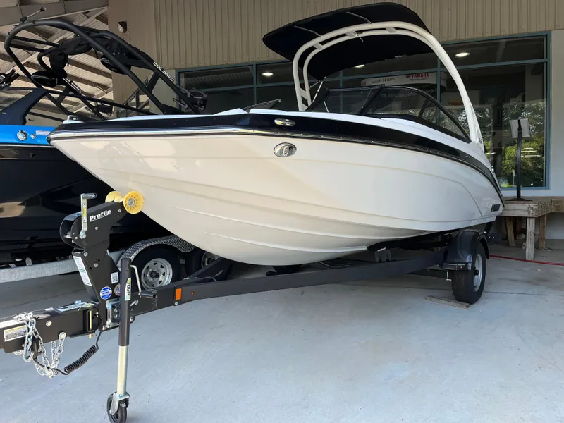 Slide: The Image of 2025 Yamaha Boats 195S on trailer, sleek white design, parked in showroom. - 1