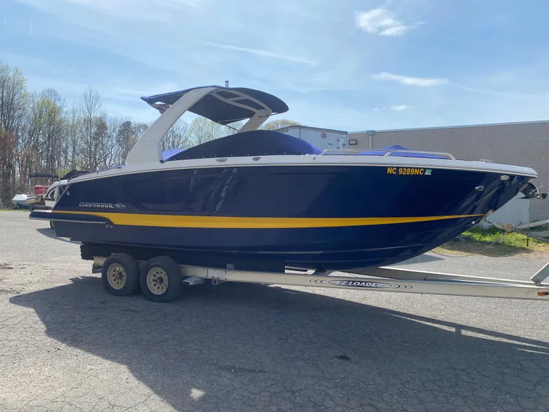 Slide: The Image of 2018 Chaparral 267 SSX boat on trailer, blue with yellow stripe, parked outdoors. - 2