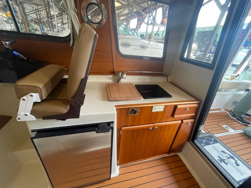 Slide: The Image of 2023 Ranger Tugs R-25 interior with kitchenette, featuring sink, fridge, and wooden cabinetry. - 22