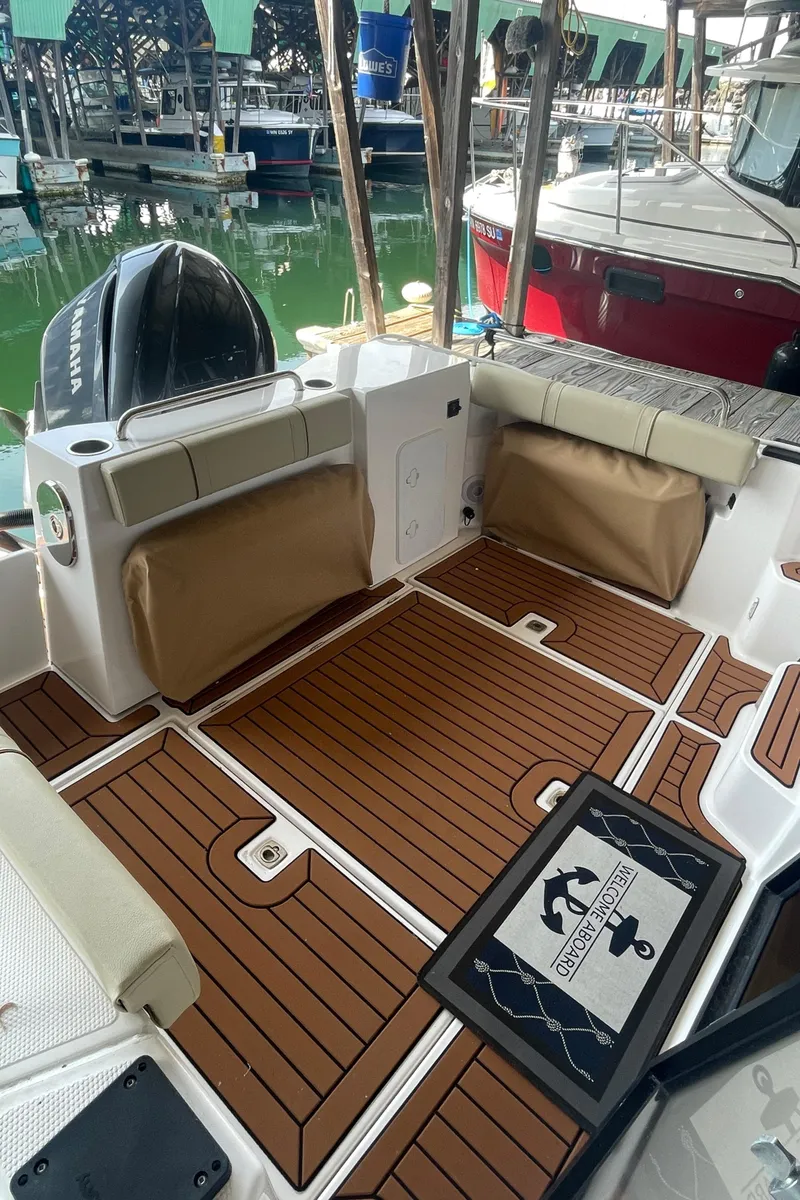 Slide: The Image of 2023 Ranger Tugs R-25 boat deck with wood finish and seating at a marina. - 3