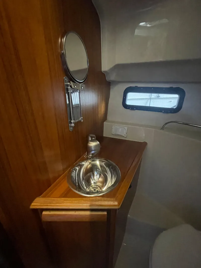 Slide: The Image of 2023 Ranger Tugs R-25 bathroom with wooden cabinetry, stainless steel sink, and porthole window. - 42