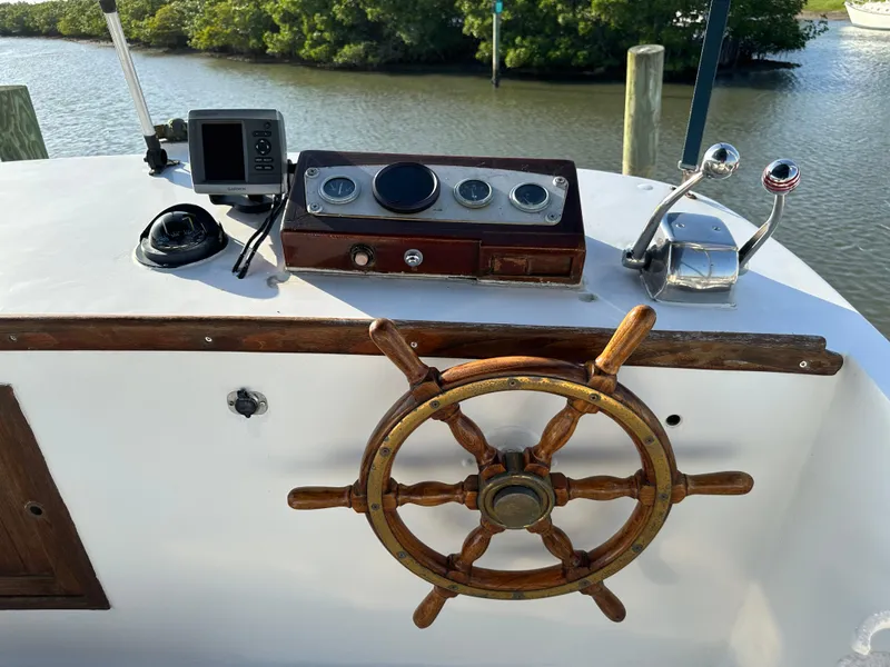 Slide: The Image of 1973 CHB Trawler helm with wooden wheel and navigation instruments, docked by a serene waterway. - 10