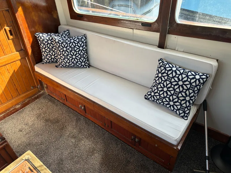 Slide: The Image of 1973 CHB Trawler interior with white cushioned bench and patterned pillows. - 15