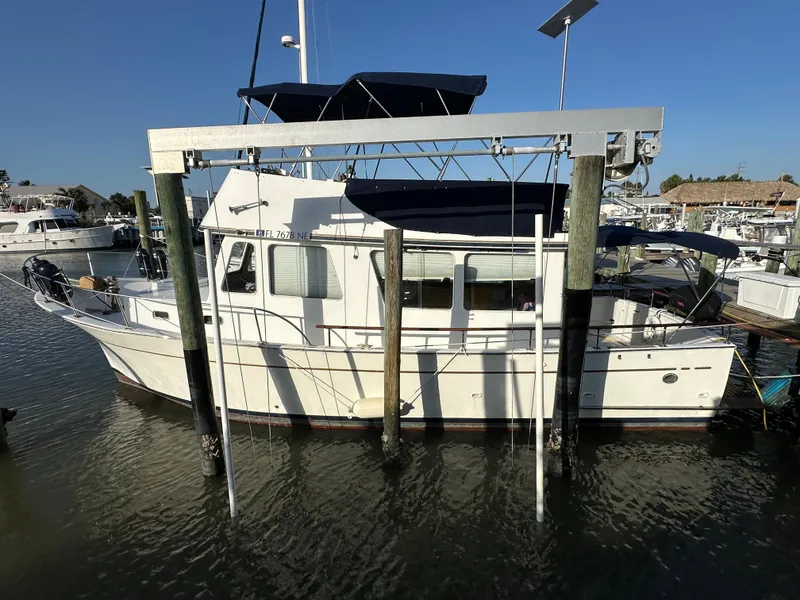 Slide: The Image of 1973 CHB Trawler docked at marina, featuring classic design and blue canopy. - 2