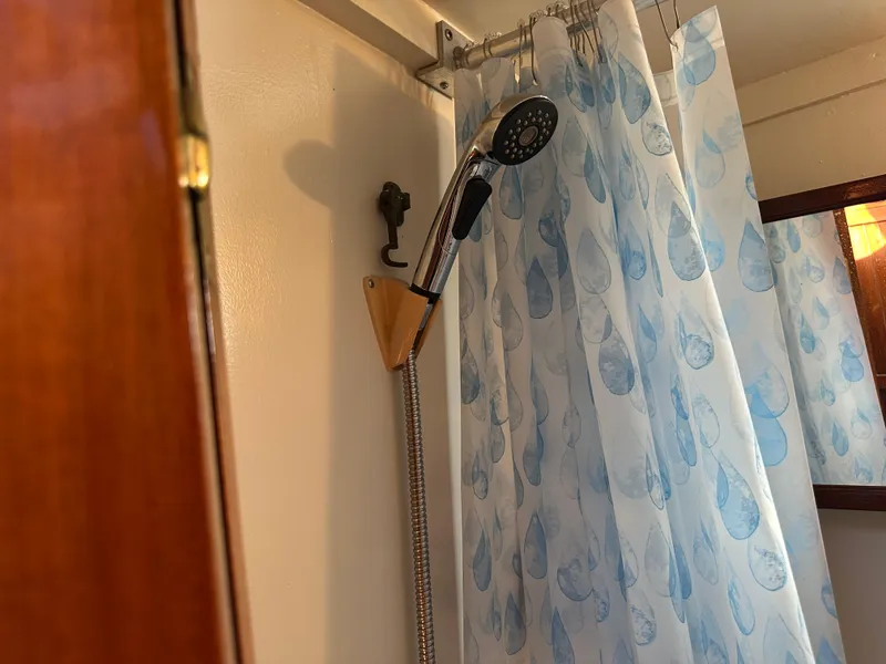 Slide: The Image of Shower area in a 1973 CHB Trawler with blue-patterned curtain and handheld showerhead. - 24