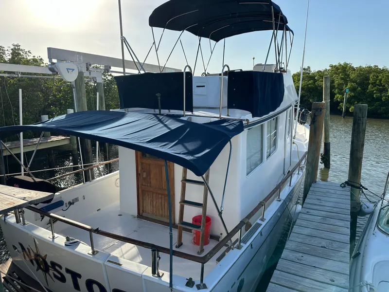 Slide: The Image of 1973 CHB Trawler docked, featuring blue canopy and wooden door, in a serene marina setting. - 3