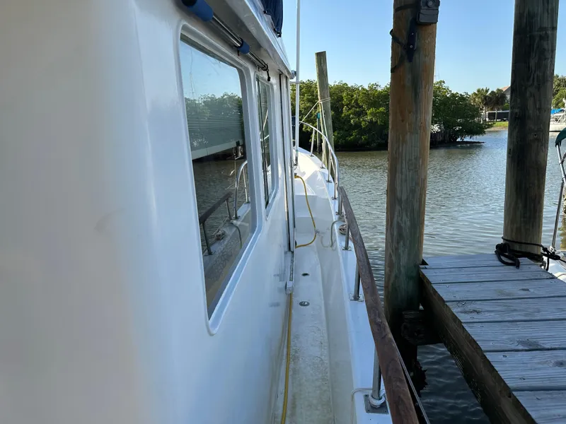 Slide: The Image of 1973 CHB Trawler docked by wooden pier, calm water, and lush greenery in the background. - 5