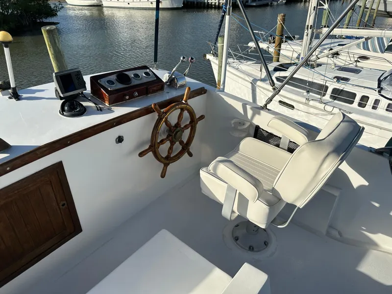 Slide: The Image of 1973 CHB Trawler helm with wooden wheel and white captain's chair, docked by the water. - 8
