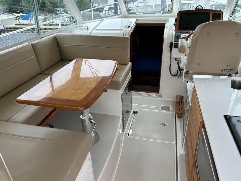 Slide: The Image of 2018 Back Cove 32 yacht interior with beige seating, wooden table, and navigation area. - 11