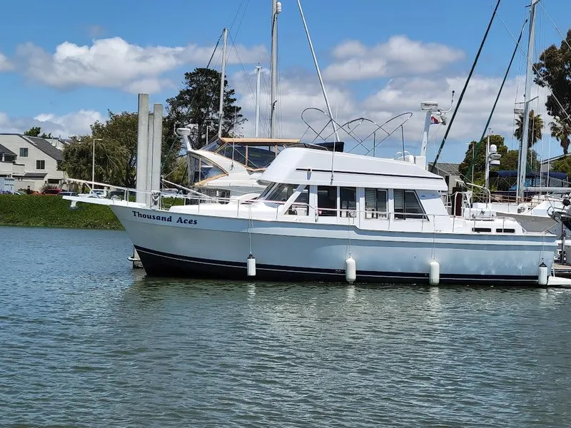 The Image of 1999 Mainship 430 Trawler docked on calm water under a blue sky. - 0