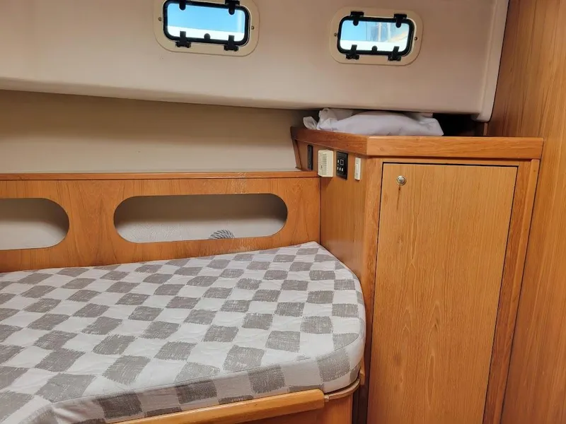 Slide: The Image of 1999 Mainship 430 Trawler cabin interior with wooden cabinetry and patterned bedding. - 38