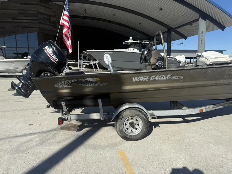 Slide: The Image of War Eagle 18 boat with Suzuki motor and American flag, parked on a trailer. - 2