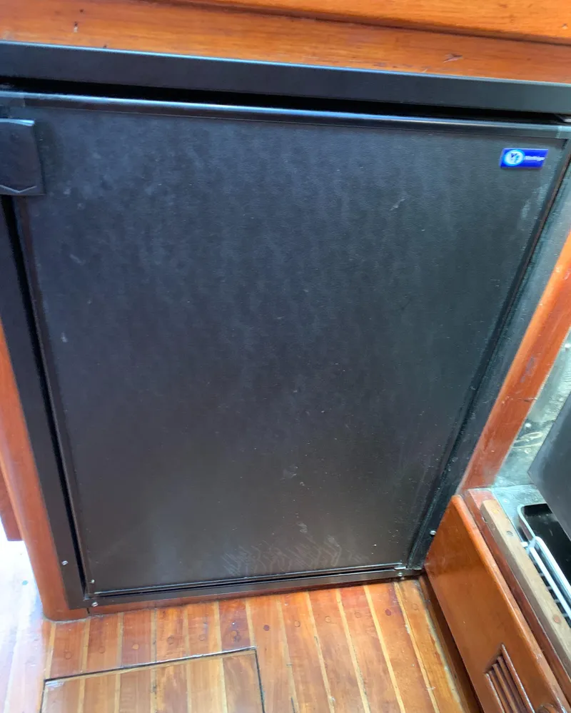 Slide: The Image of 1979 Robert Perry 41 Sloop interior with wooden flooring and compact black refrigerator. - 41