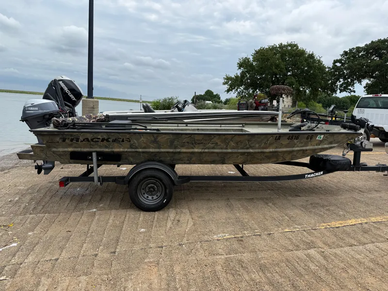Slide: The Image of 2017 Tracker Grizzly 1654 MVX Sportsman boat on trailer by a lake. - 12