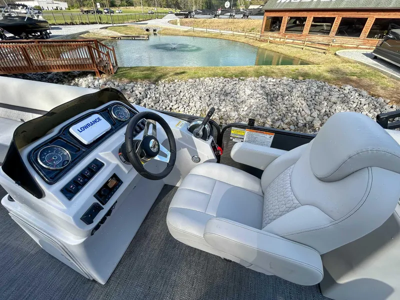 Slide: The Image of 2022 Godfrey Sweetwater boat helm with Lowrance display, luxurious seating, and scenic pond view. - 10
