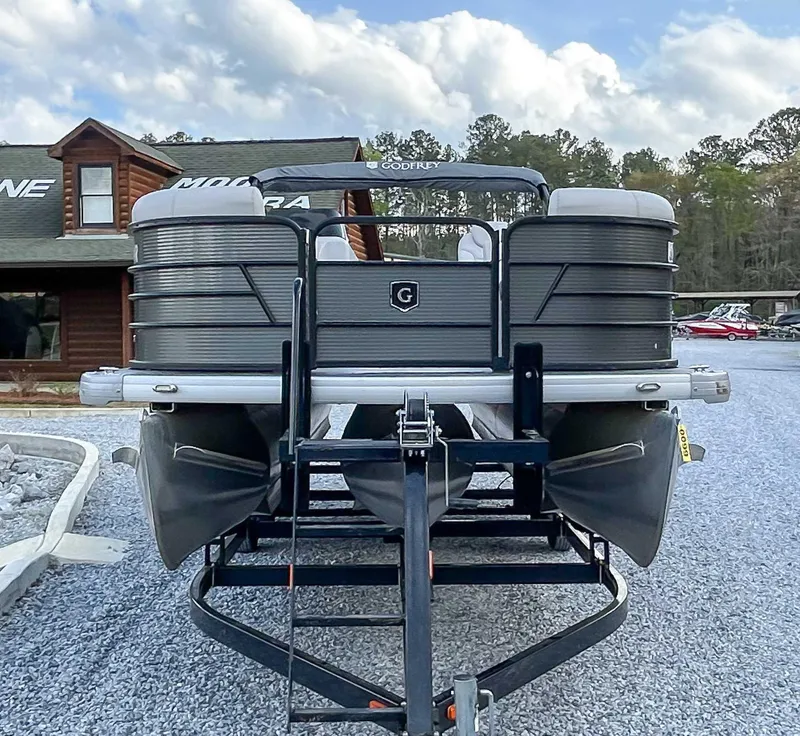 Slide: The Image of 2022 Godfrey Sweetwater pontoon boat on trailer, parked on gravel near wooden building. - 3