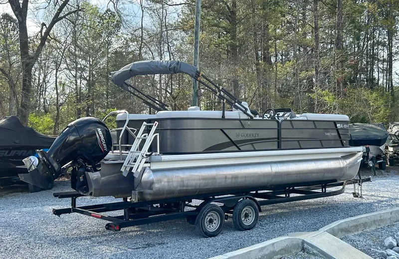 Slide: The Image of 2022 Godfrey Sweetwater pontoon boat on trailer, parked in wooded area. - 5