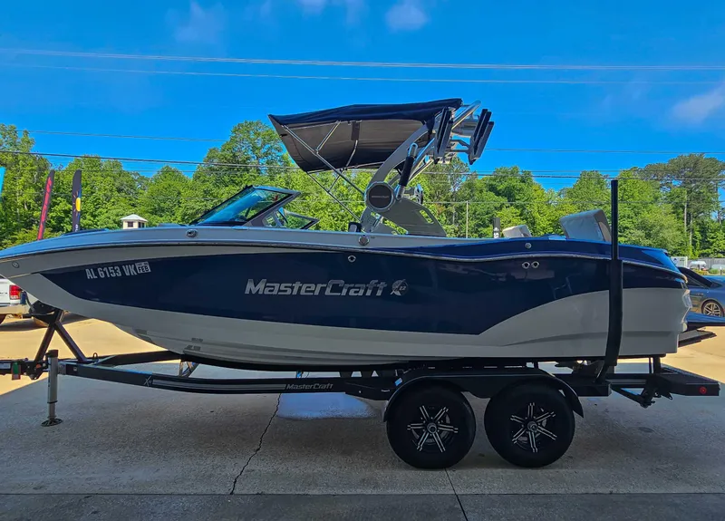 Slide: The Image of 2021 MasterCraft X22 boat on trailer, parked outdoors under clear blue sky. - 6