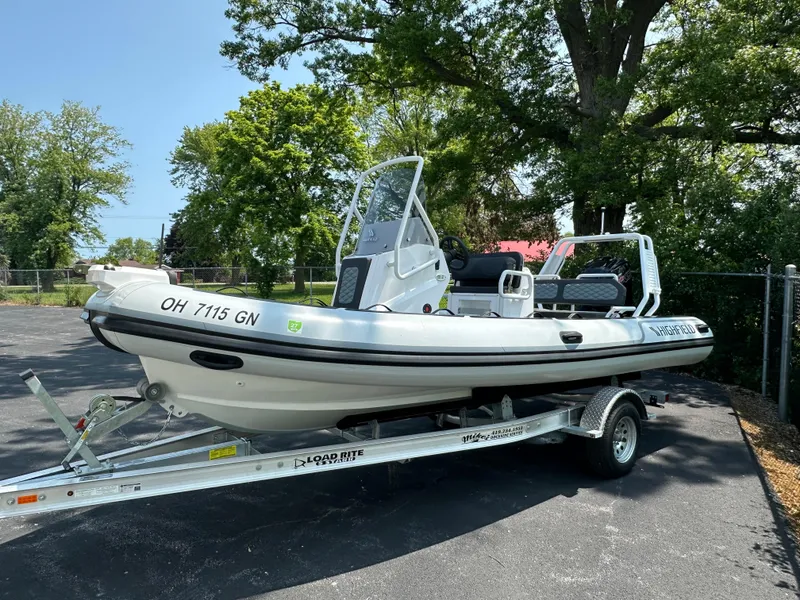 Slide: The Image of 2025 Highfield Sport 560 boat on trailer, parked outdoors with trees in background. - 2