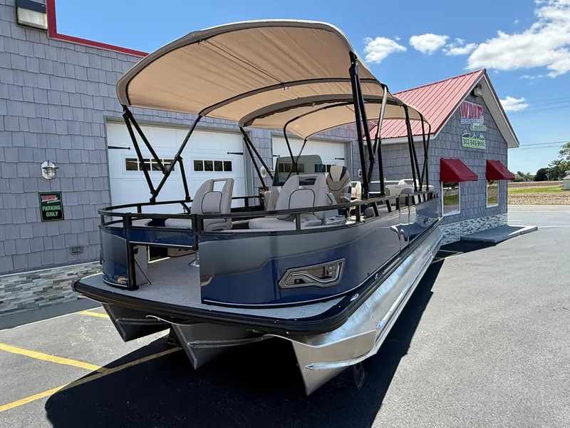 Slide: The Image of 2025 Avalon 2585 Venture 85 Tri Toon boat with center console, parked outside a building. - 3