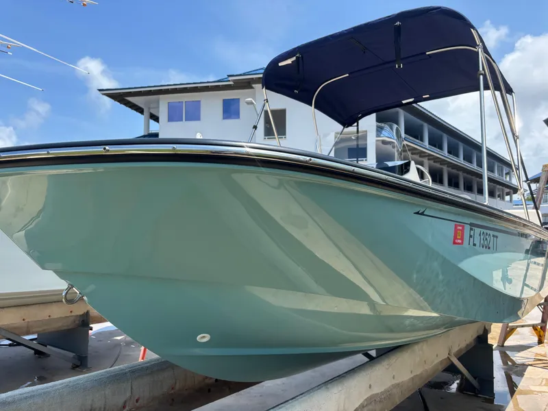 Slide: The Image of 2024 Boston Whaler 170 Montauk boat with blue canopy, docked near modern building. - 1