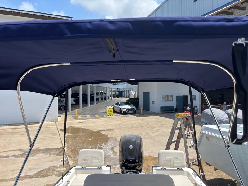 Slide: The Image of 2024 Boston Whaler 170 Montauk with blue canopy in a boatyard setting. - 19