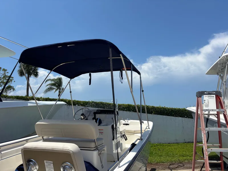 Slide: The Image of 2024 Boston Whaler 170 Montauk boat with canopy, parked outdoors under a clear blue sky. - 23