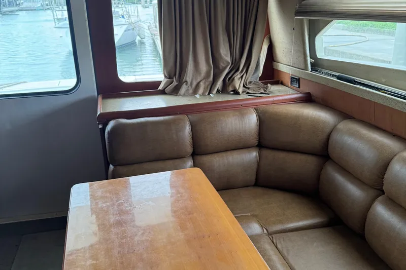 Slide: The Image of 2004 Luhrs 36 Convertible interior with brown leather seating and wooden table by a window. - 18
