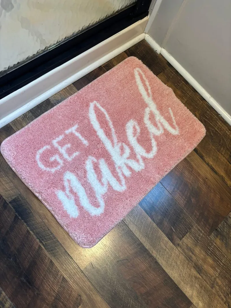Slide: The Image of Pink bath mat with "Get Naked" text on wooden floor. - 10