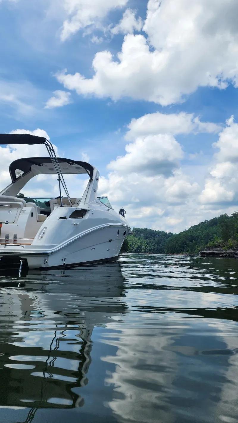 Slide: The Image of 2010 Sea Ray 310 Sundancer on a serene lake under a partly cloudy sky. - 2