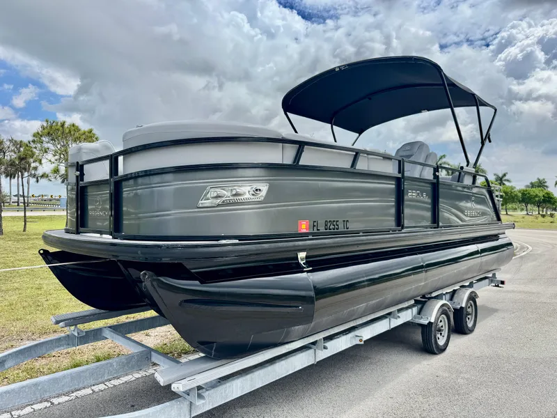 Slide: The Image of 2022 Regency 230 LE3 Sport pontoon boat on trailer under cloudy sky. - 2