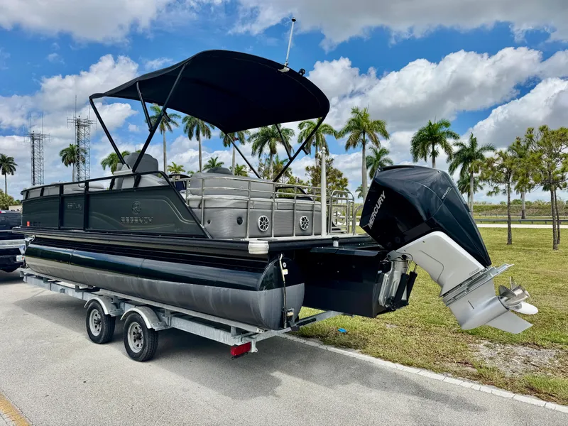 Slide: The Image of 2022 Regency 230 LE3 Sport pontoon boat on trailer, parked near palm trees under a cloudy sky. - 4